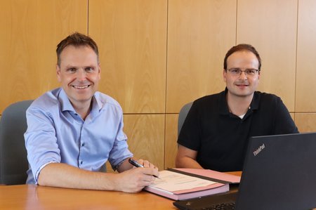 Zwei Personen sitzen an einem Tisch mit einer Unterschriftenmappe