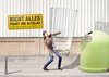 Symbolbild, auf dem eine Frau ein riesiges Glas zum Altglascontainer trägt