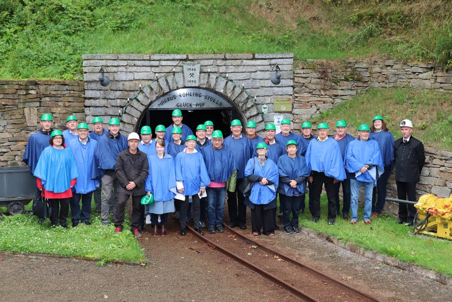 Gruppe mit Personen mit Schutzkleidung und Helm vor dem Stolleneingang