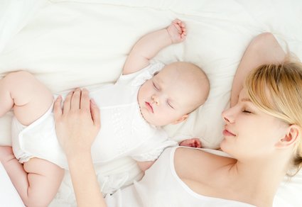 Mutter liegt mit Baby auf dem Bett und schläft